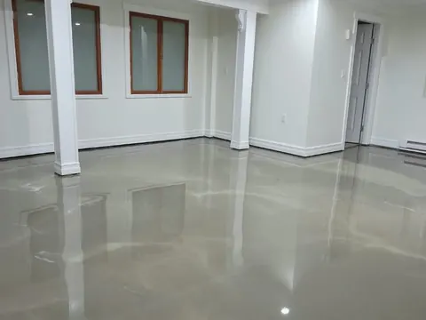 Basement after a self-levelling pour, the glossy grey surface reflecting the pot lights